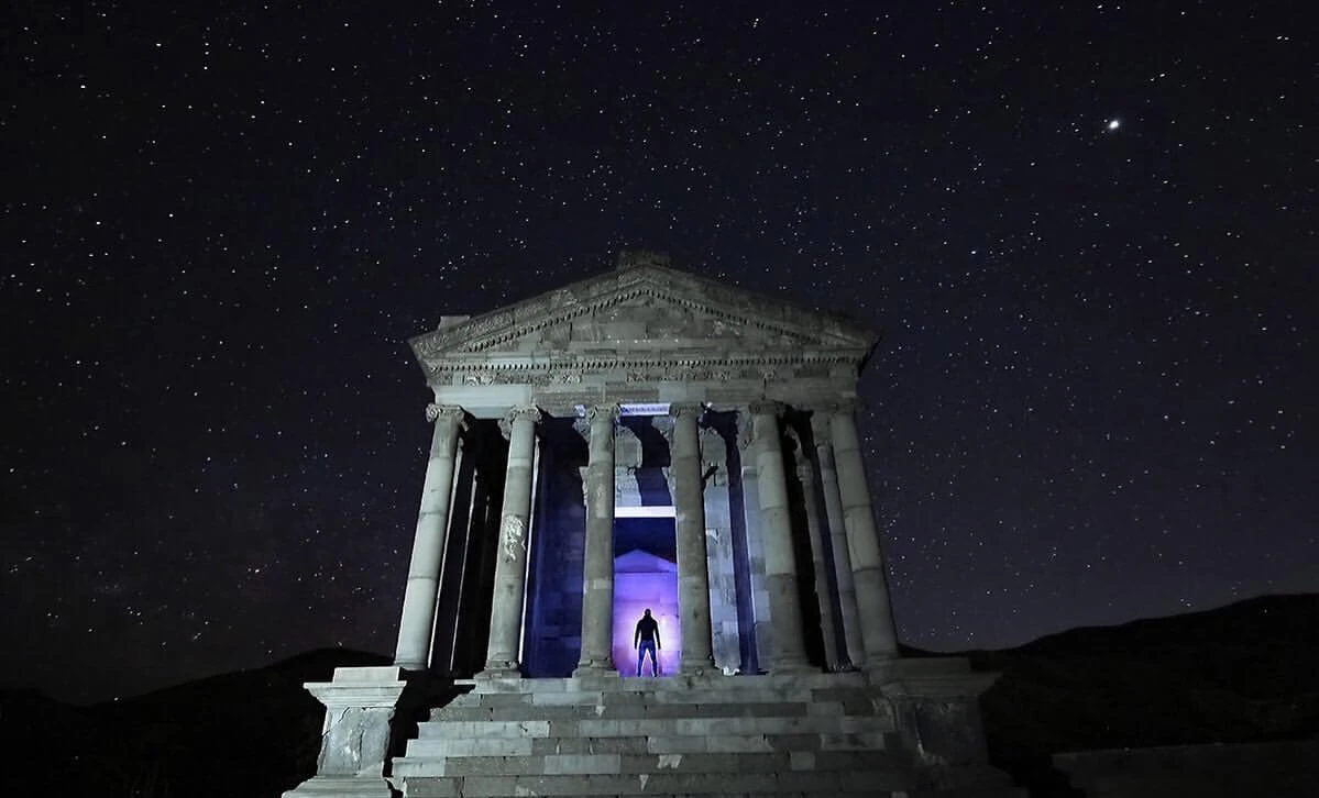 The Temple of Garni lit at night under a star-filled sky